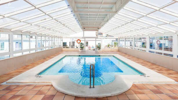 An indoor swimming pool with a tiled floor, glass ceiling, and a lifeguard stand. - Port Fiesta Park Hotel (Benidorm)