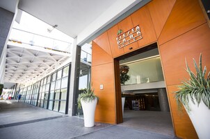 Ingresso moderno di un hotel con facciata in legno, grandi piante in vaso e un corridoio in vetro.