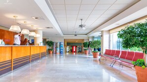 A hotel lobby with a reception desk, seating area, ceiling fans, and potted plants. - Port Fiesta Park Hotel (Benidorm)