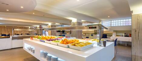 Uma área de buffet com diversas frutas e um balcão com pilhas de pratos.