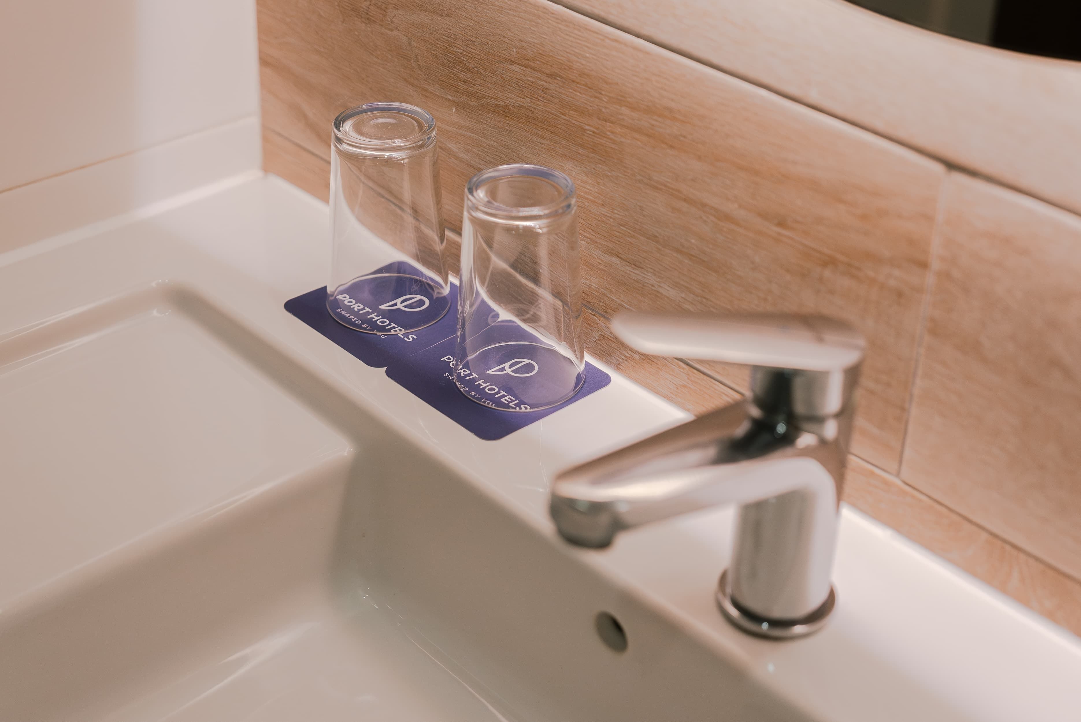 Un lavabo de bany amb dos vasos de vidre transparent sobre un reposacristalls morat, un aixeta modern i una paret de fusta.