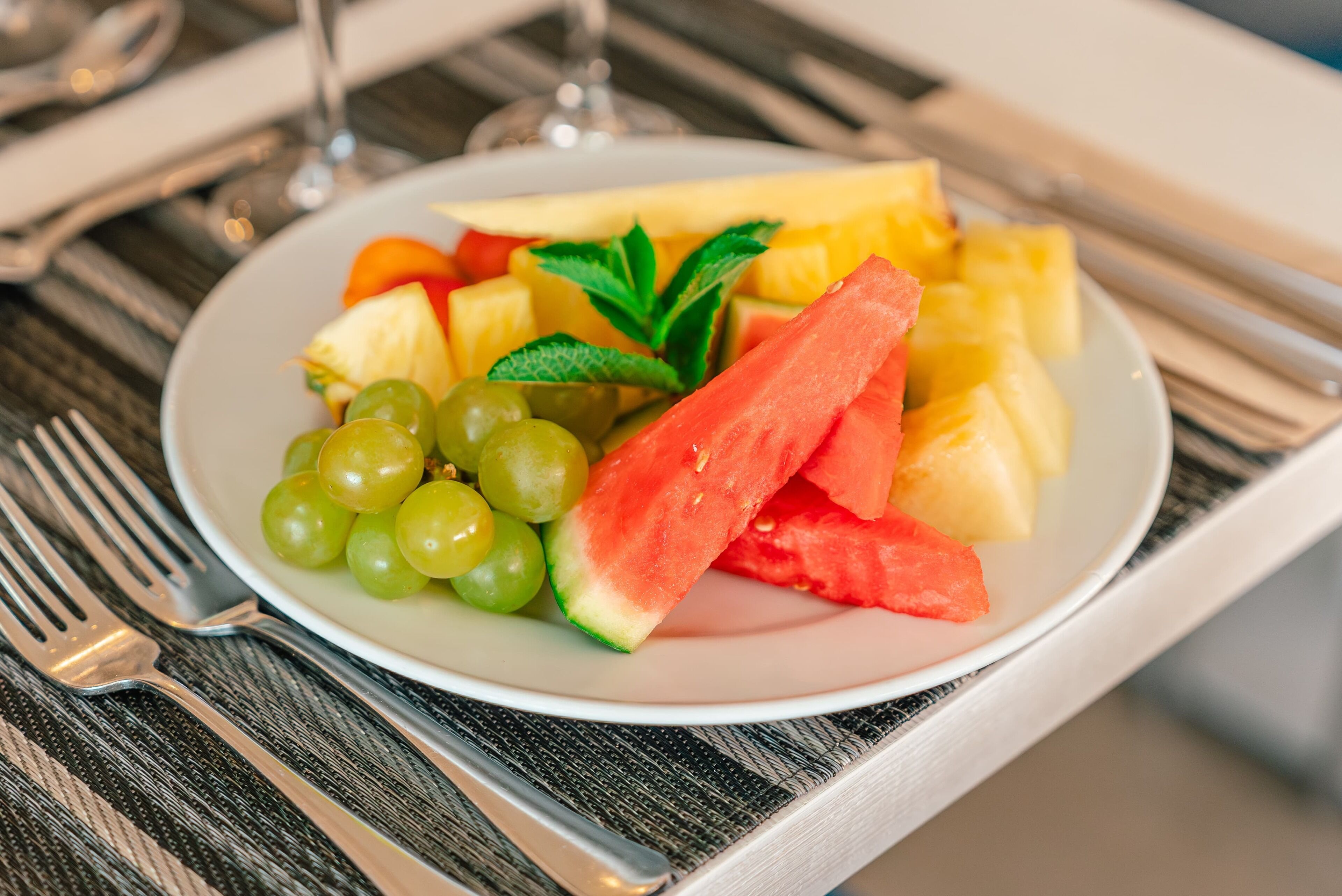 A plate of fruit including watermelon, pineapple, and grapes, with a fork and knife on a table.