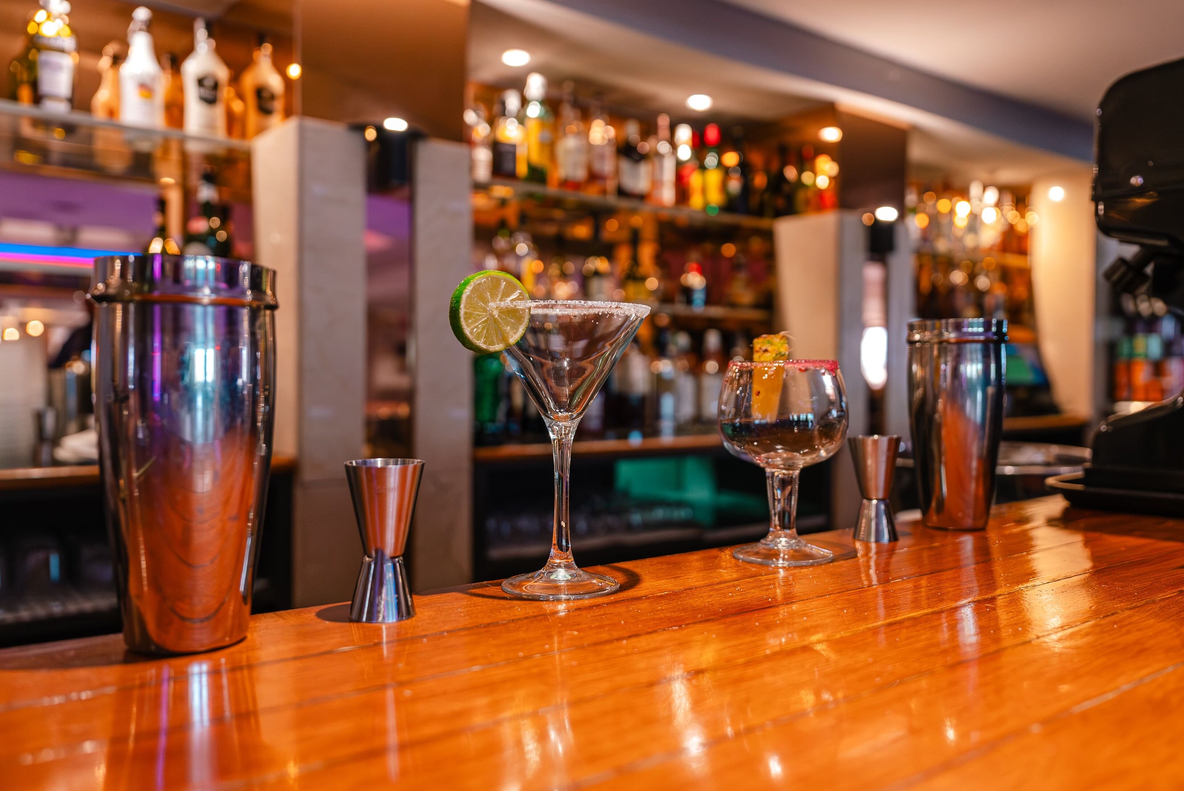 A bar area with various cocktail shakers and glasses on a wooden counter.