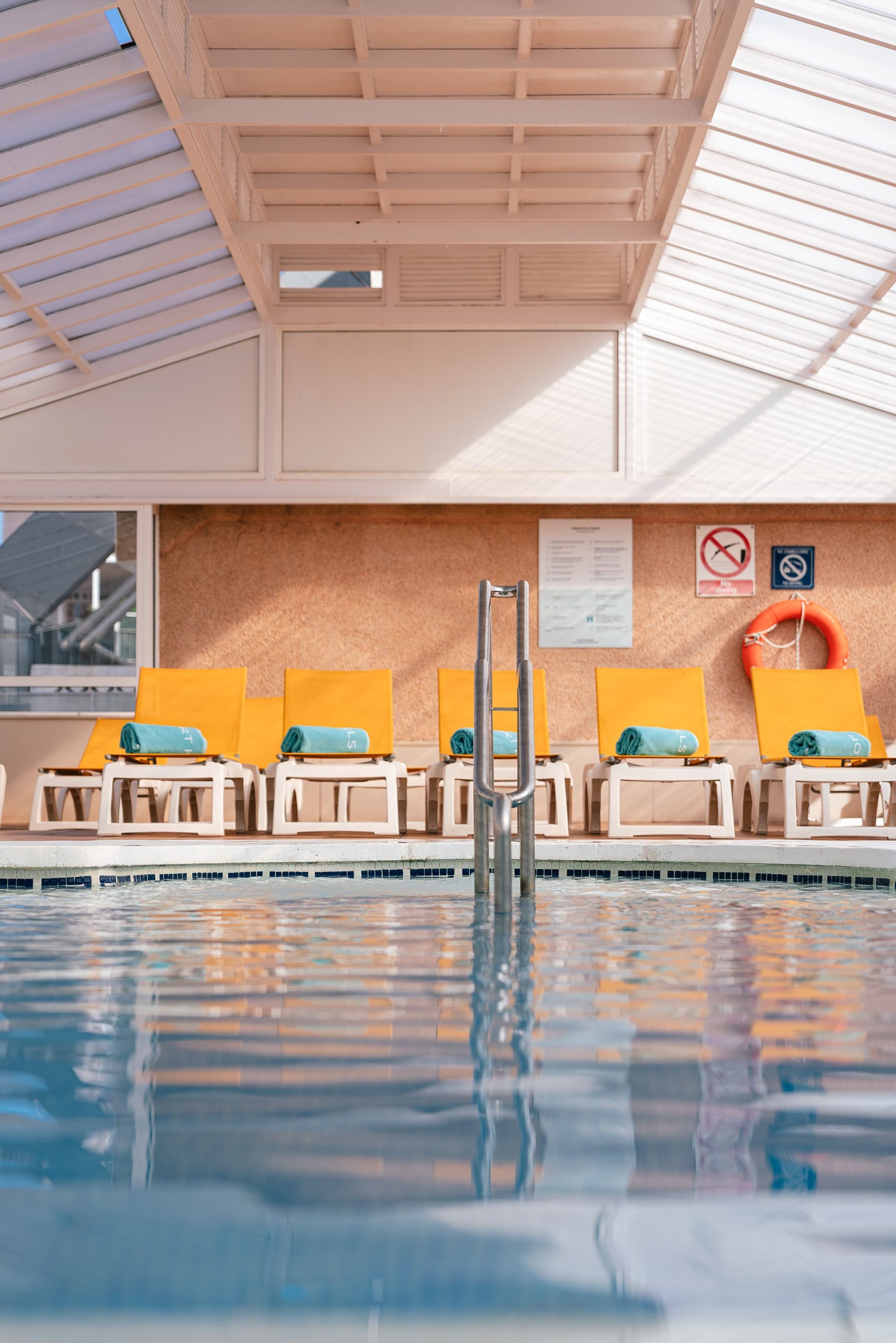 A swimming pool with sun loungers, a ladder, and safety signs.