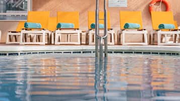 A swimming pool with sun loungers, a ladder, and safety signs.