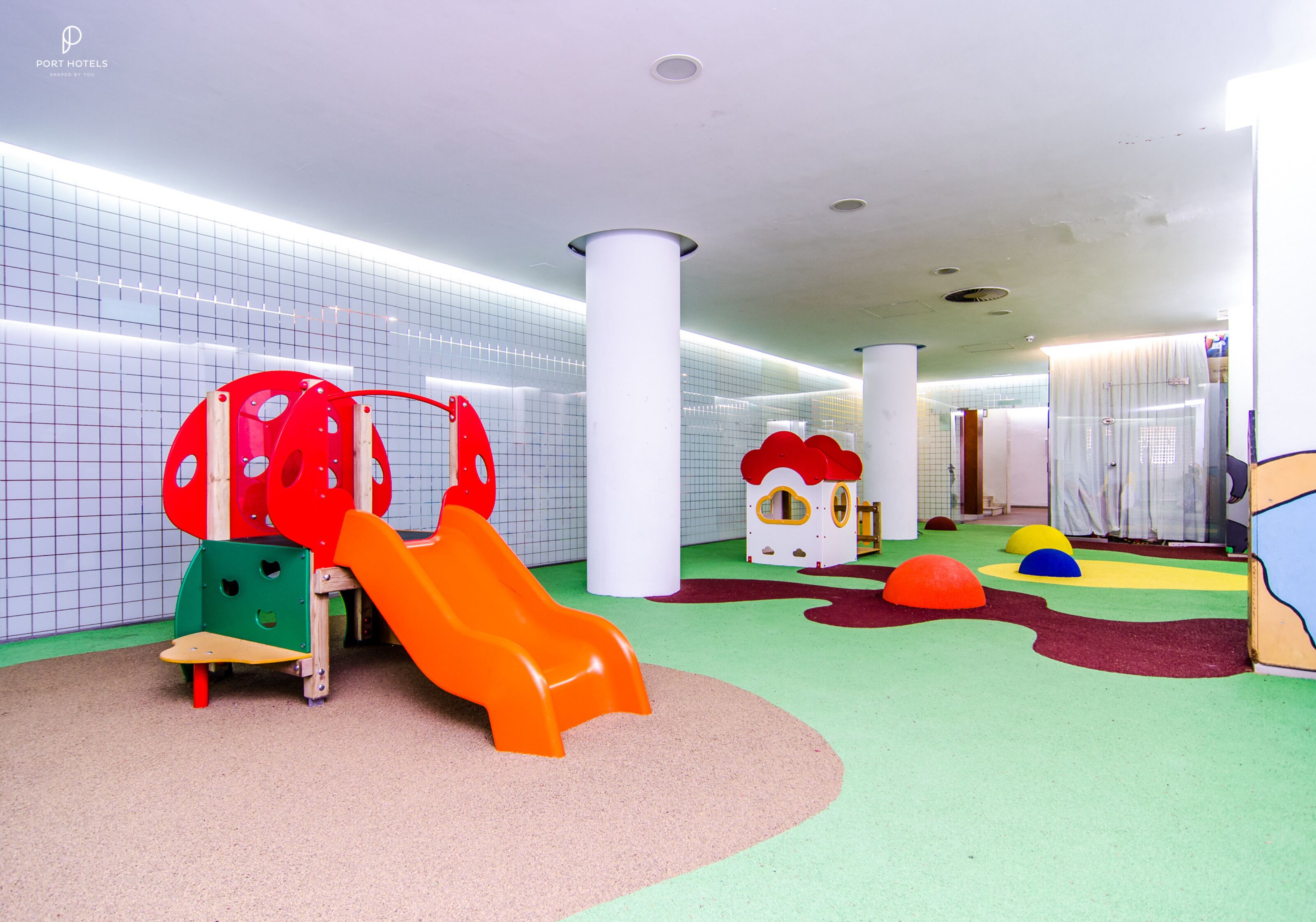 A children's play area with a slide, colorful play structures, and soft play mats.