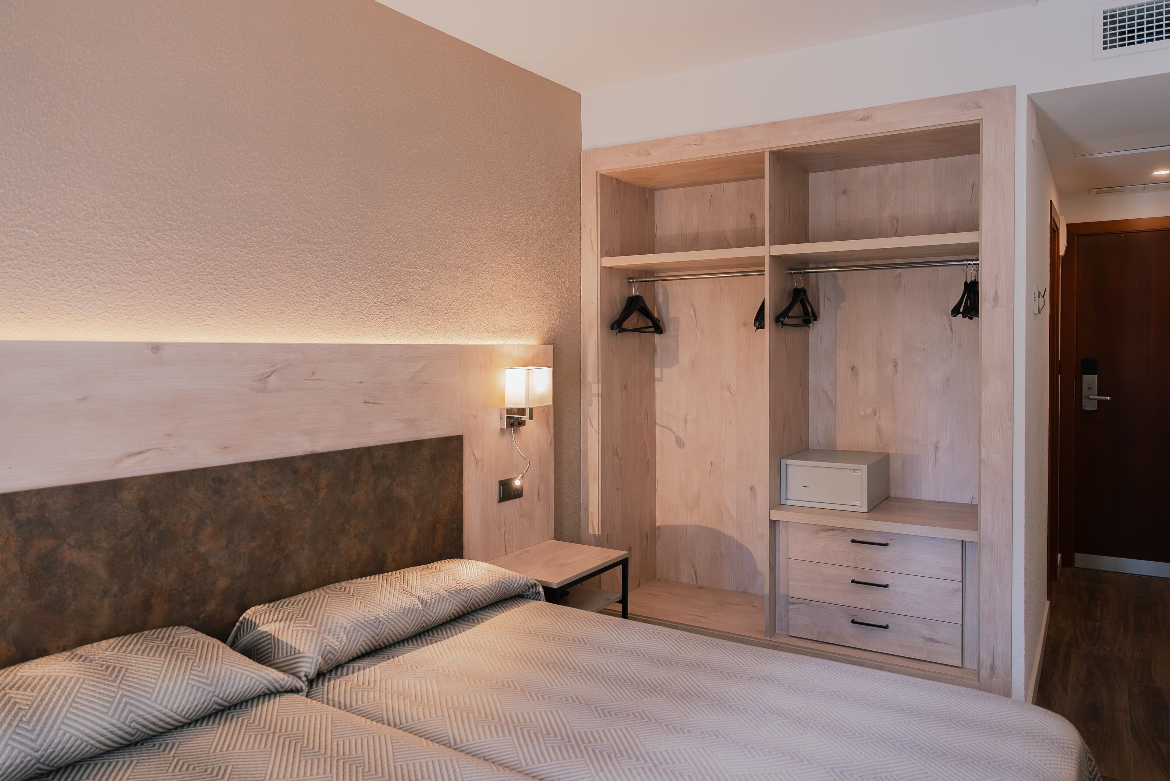 Un dormitorio con una cama, una mesita de noche, un armario de madera con espacio para colgar y un mueble pequeño.