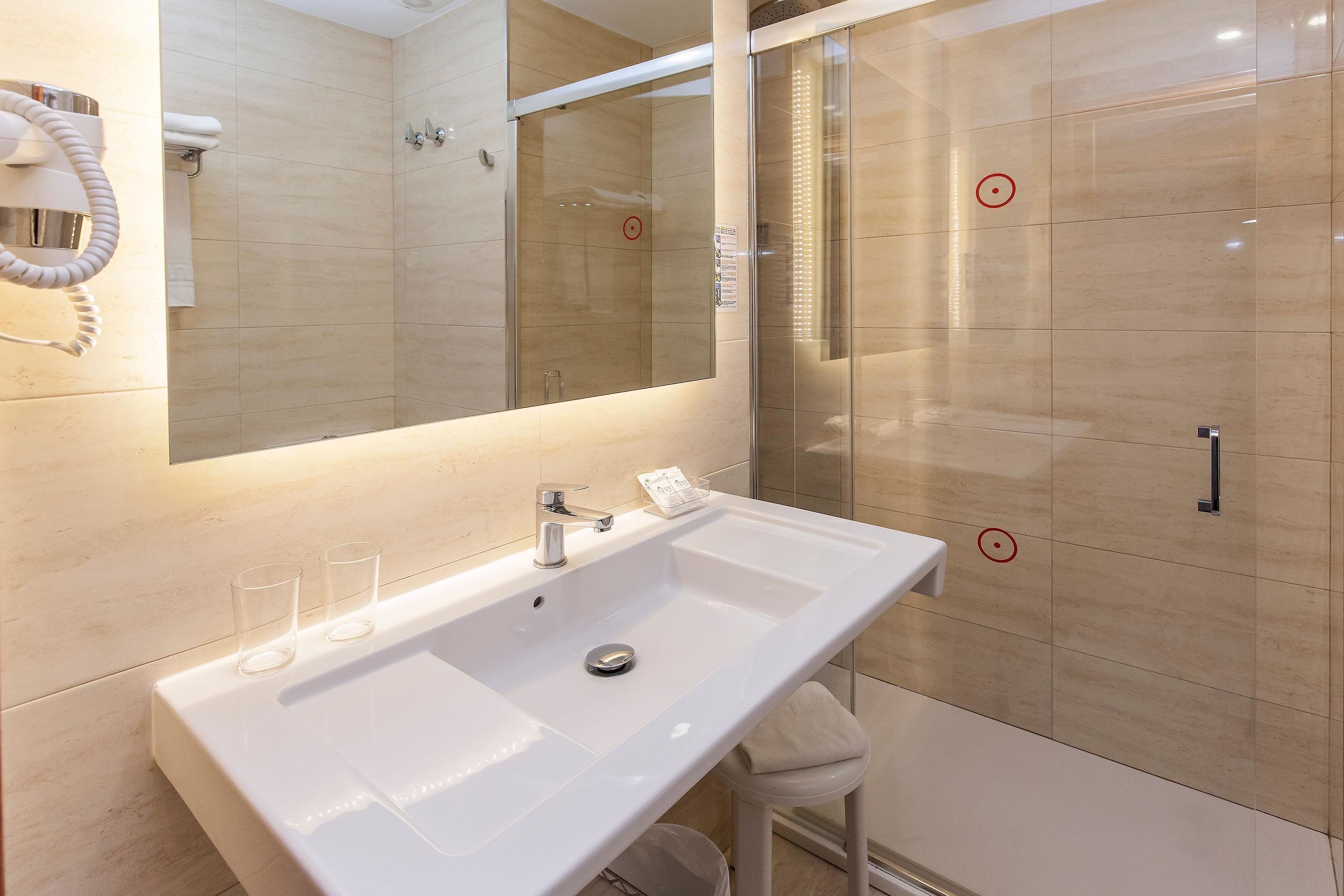 A modern bathroom with a large mirror, a white sink, and a glass-enclosed shower.