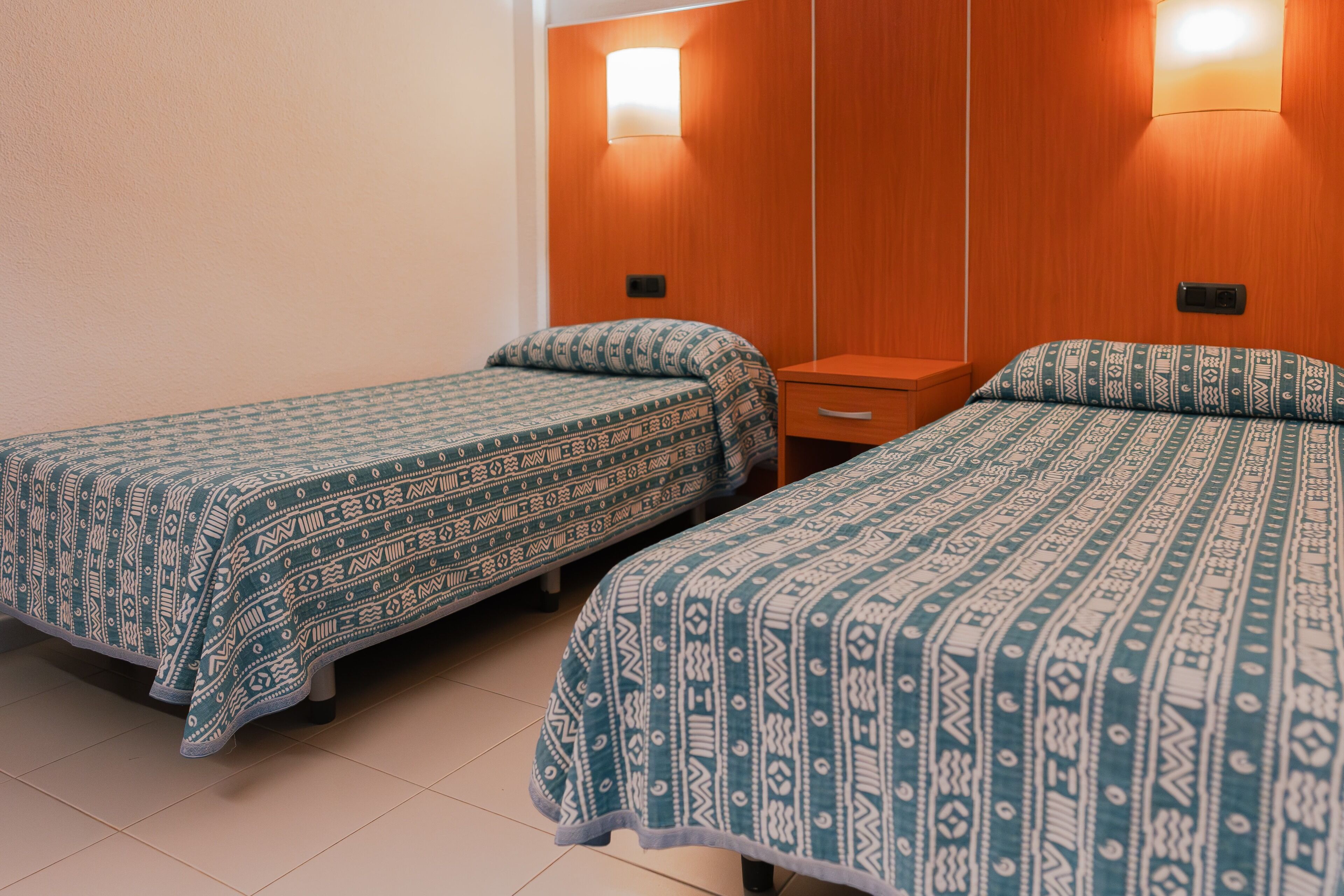 Two single beds with patterned bedding in a room with wooden headboards and bedside lamps.
