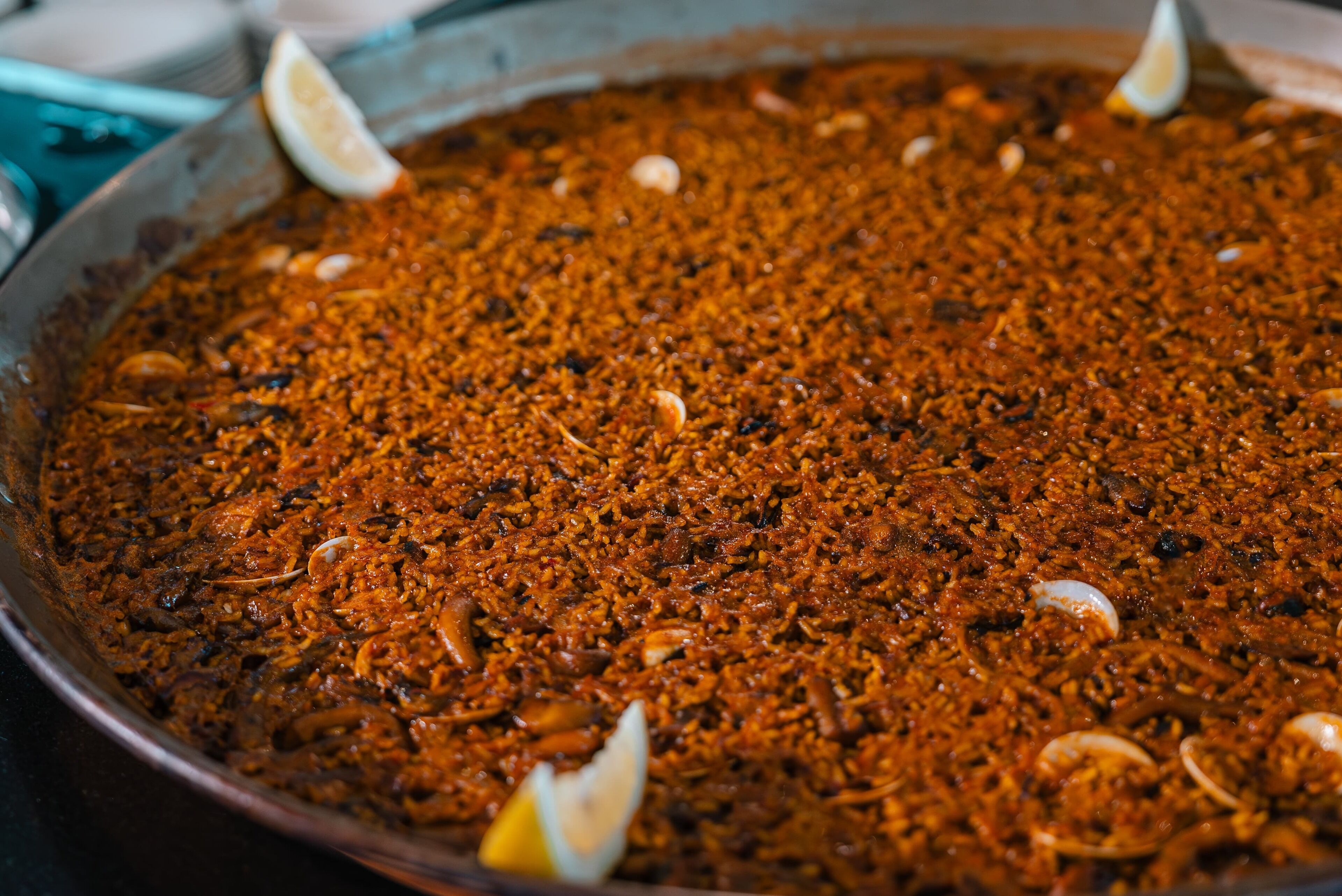 Un grand plat de service rond en métal, rempli d’un plat épais de couleur brun rougeâtre, garni de tranches de citron et de fruits de mer.