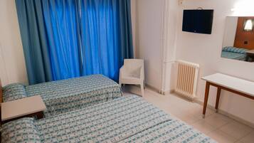 Una habitación de hotel con una cama, una silla, un escritorio, un televisor y una ventana con cortinas.