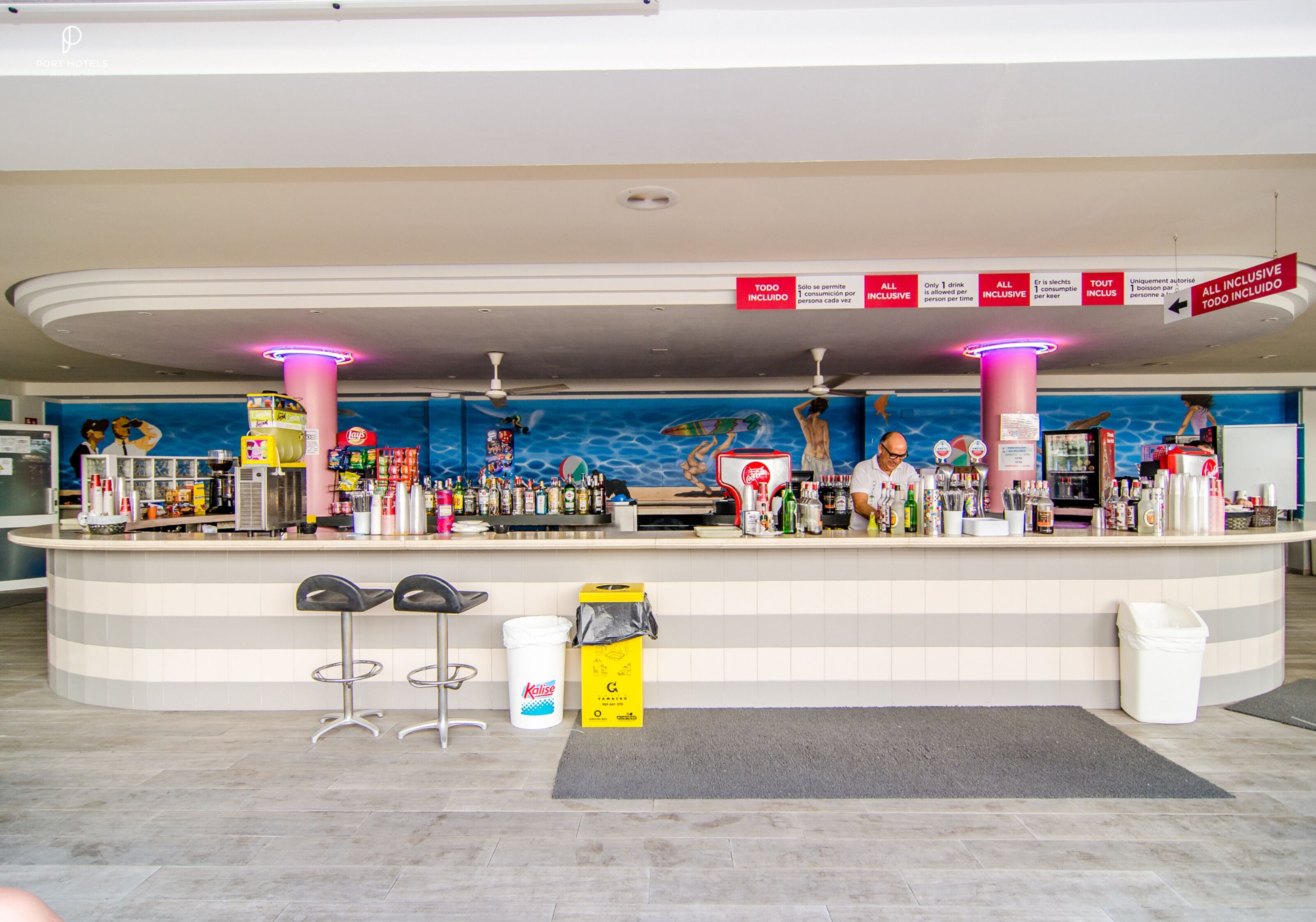 A hotel reception area with a counter, bar stools, a trash bin, and a water dispenser.