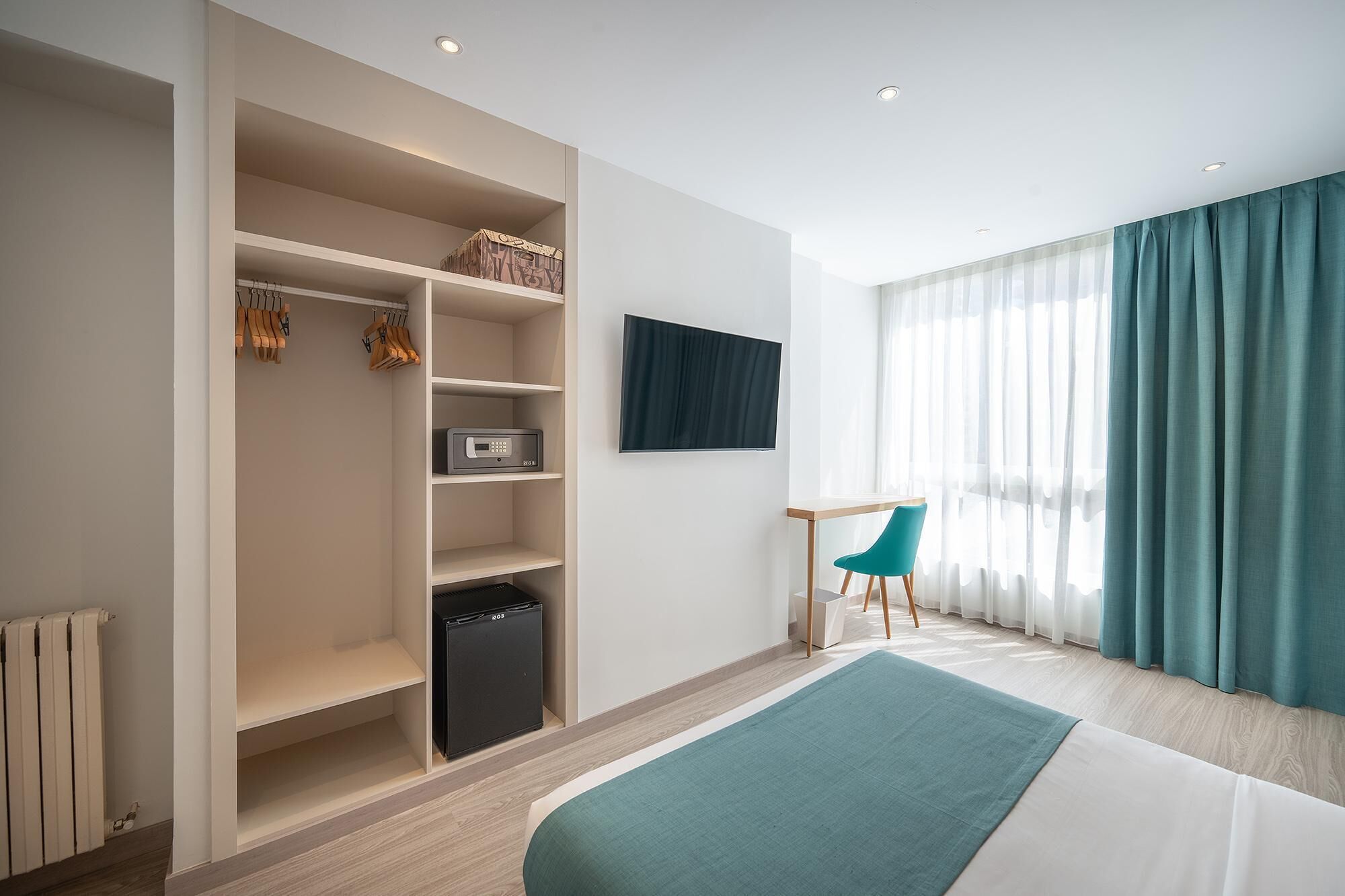 Une chambre à coucher moderne, comprenant un lit, un bureau, une chaise, une armoire et un téléviseur.