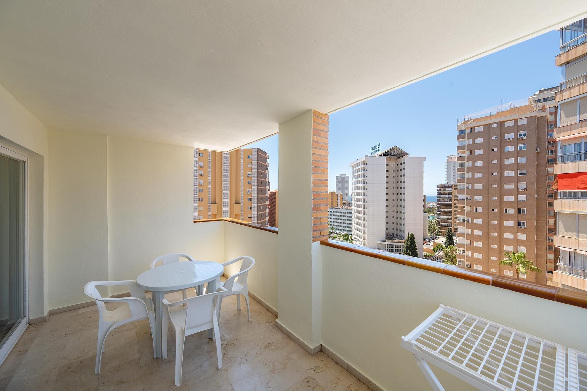 A balcony with a table and chairs, a view of high-rise buildings, and a clear sky.