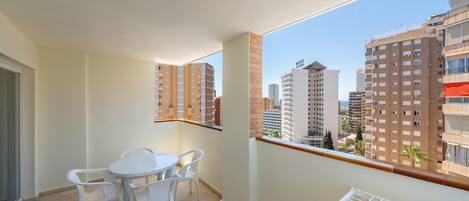 A balcony with a table and chairs, a view of high-rise buildings, and a clear sky.