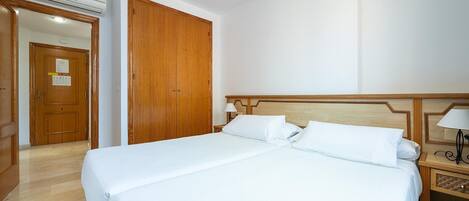 Una habitación de hotel con una cama grande, un armario de madera y una mesita de noche con una lámpara.