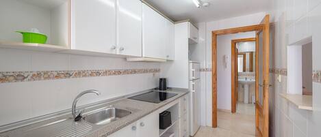 Una cocina compacta con armarios blancos, encimera de granito y horno integrado.