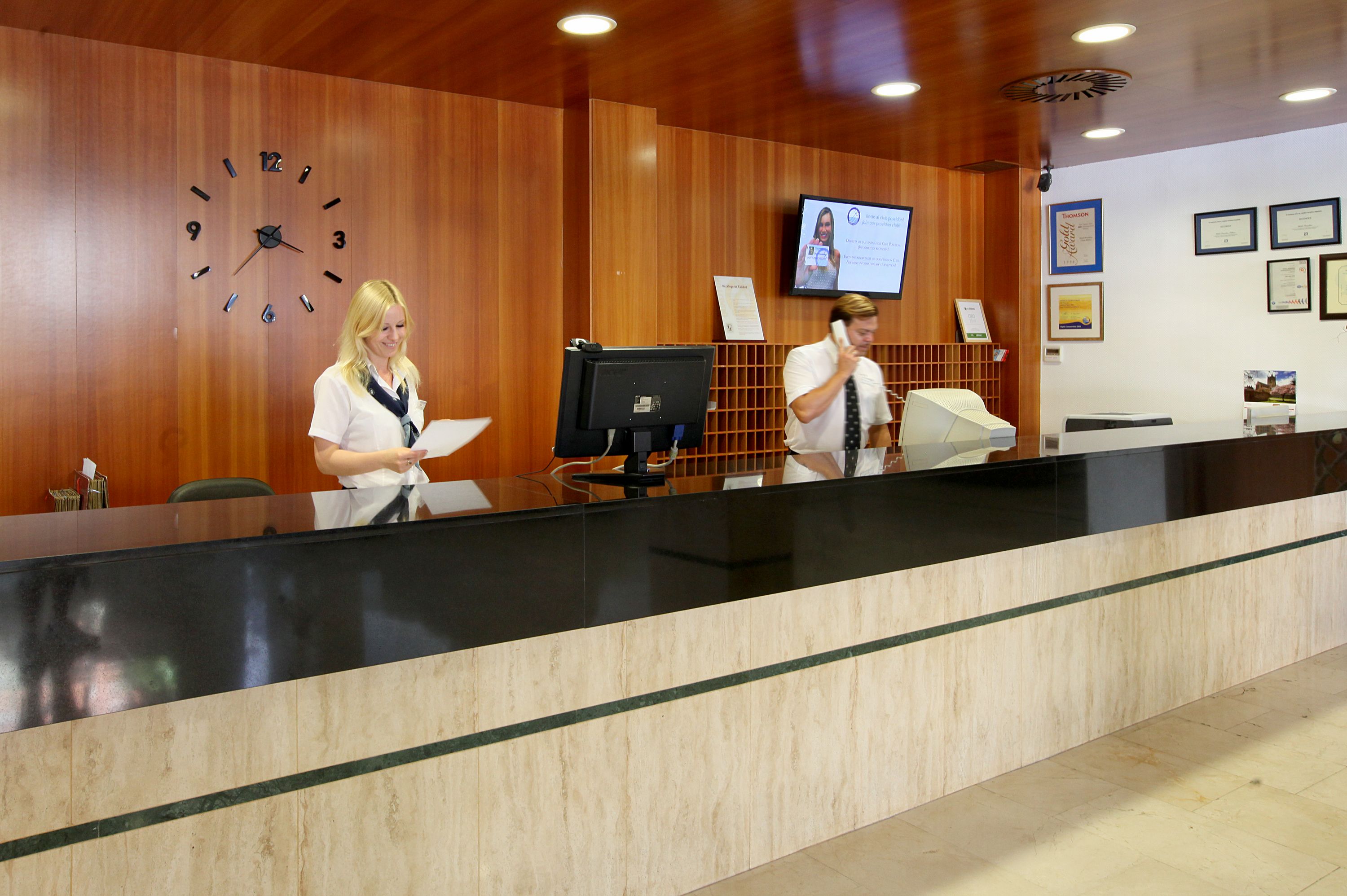Un comptoir d’accueil avec un mur revêtu de panneaux en bois, une horloge, un écran de télévision et des certificats encadrés.