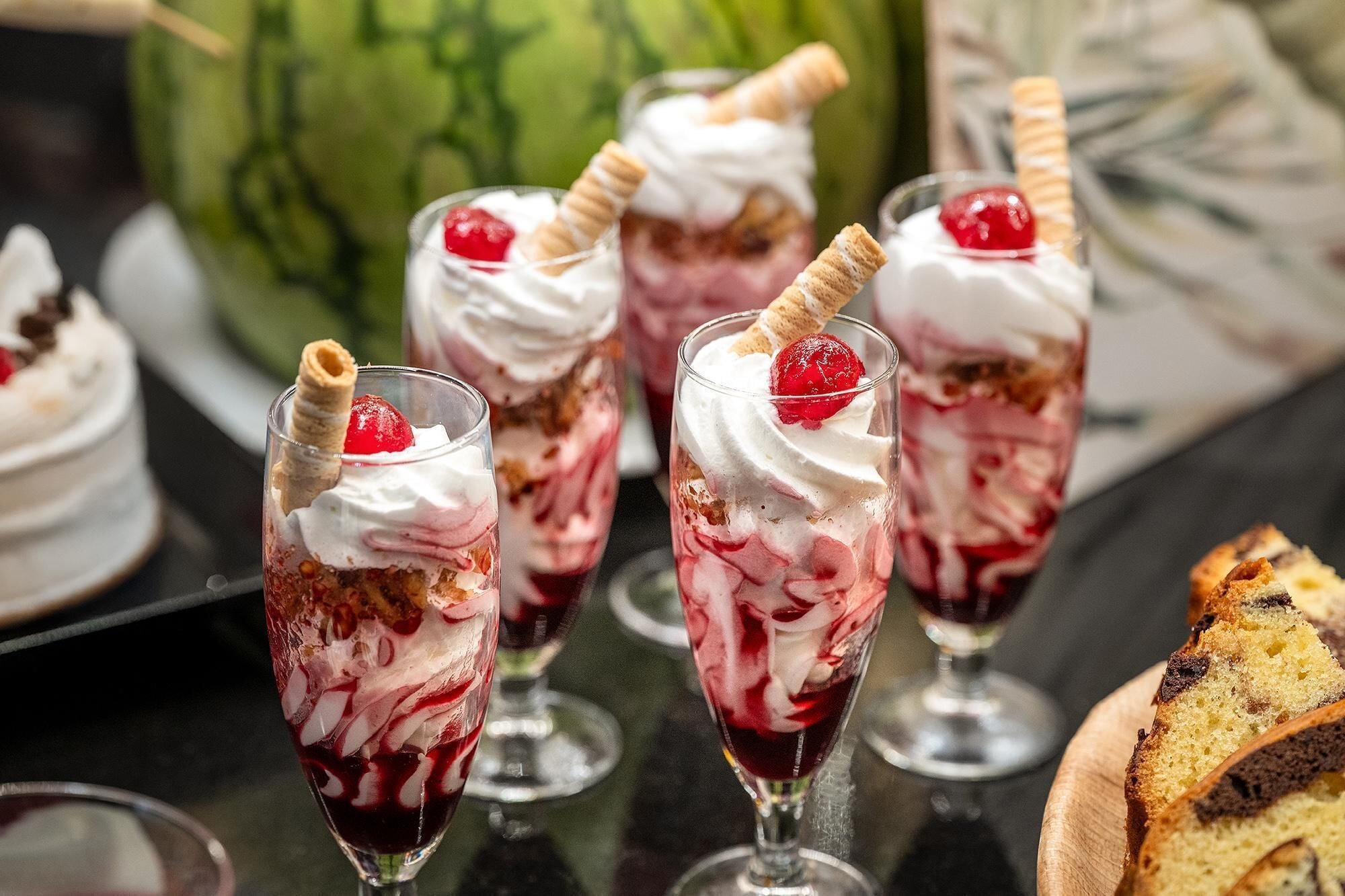 A dessert display with layered cakes and whipped cream, garnished with cherries and wafer sticks.