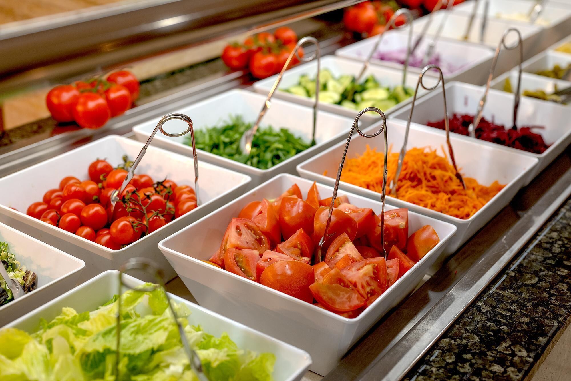 A buffet with various food options including tomatoes, lettuce, and other vegetables.