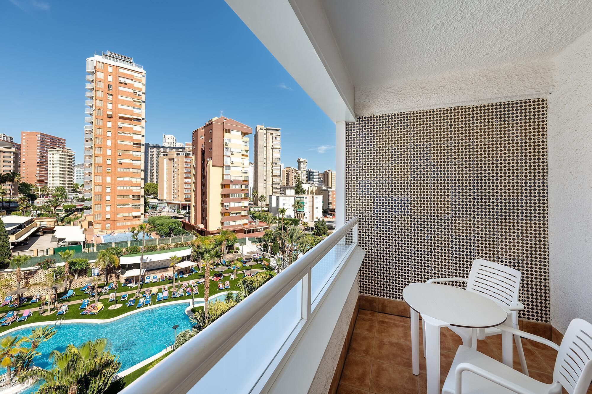 Un balcon donnant sur la piscine, avec des chaises blanches et un mur orné de motifs.