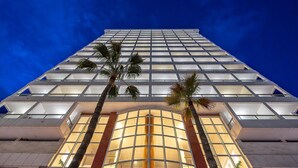 A high-rise building with a modern glass facade, palm trees in front, and a central entrance with a glass door. - Poseidon Resort (Benidorm)