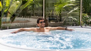 A man relaxing in a hot tub with a tropical garden view. - Poseidon Resort (Benidorm)