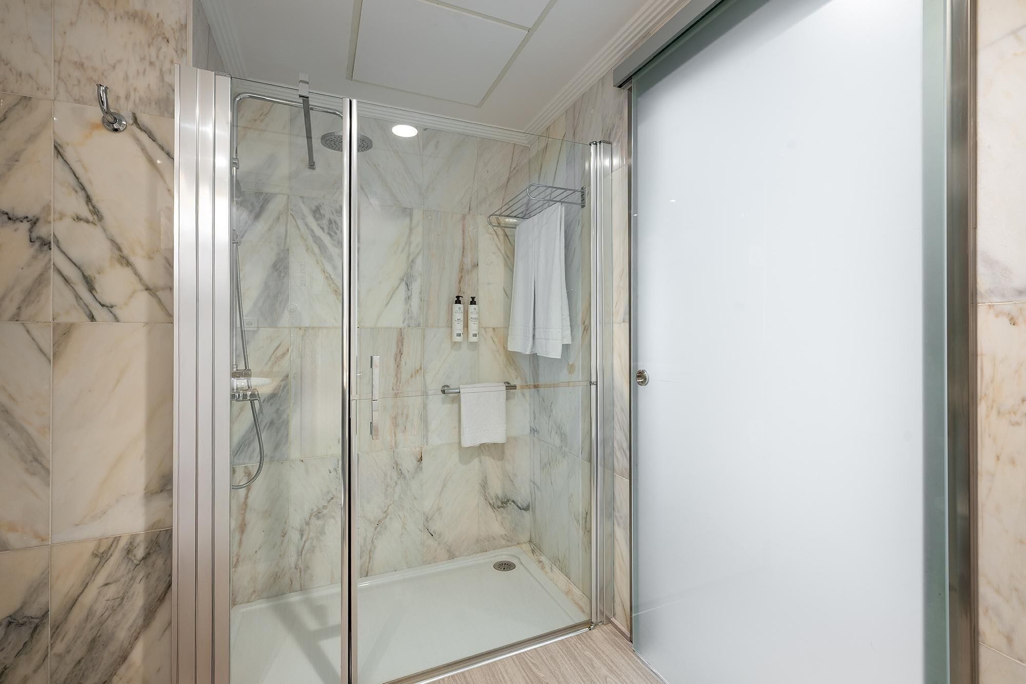 A glass-enclosed shower with a marble wall, a white towel, and a glass door.
