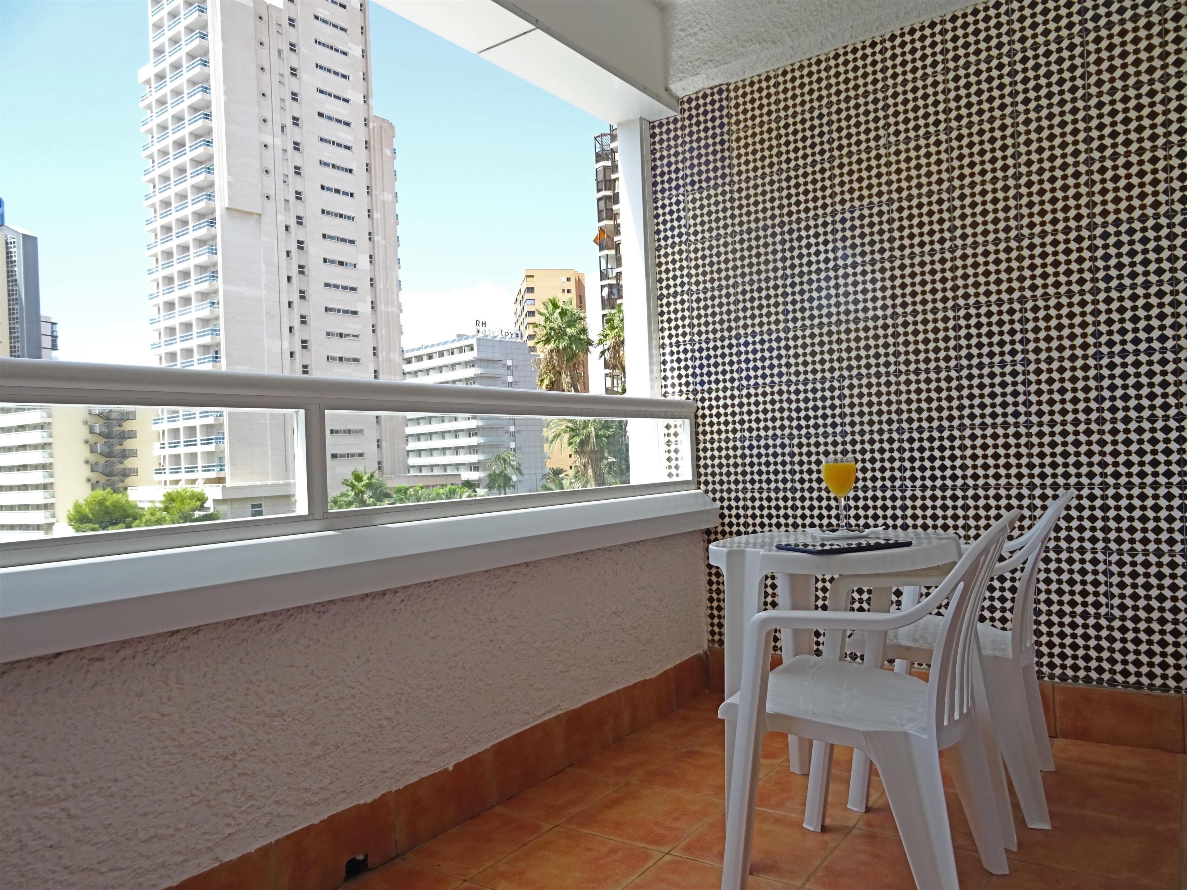 Un balcon avec une table et des chaises, un mur décoré de motifs et une vue sur les immeubles de la ville.