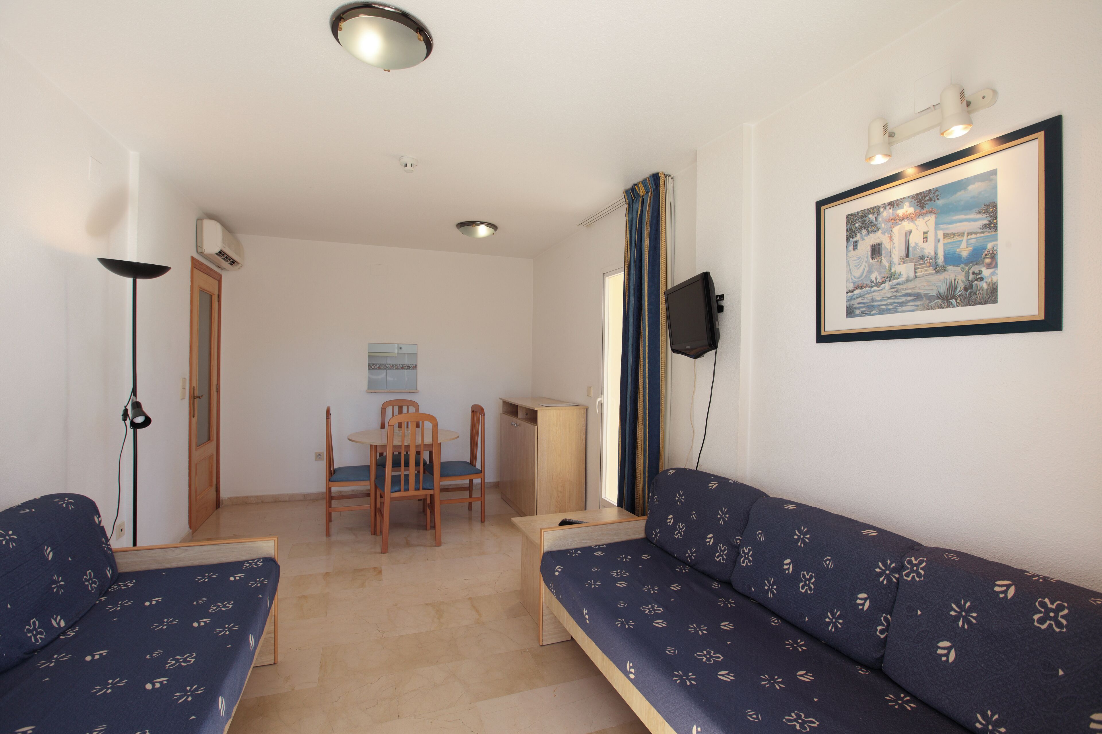 A compact living space with a sofa, a small table, a chair, and a television mounted on the wall.