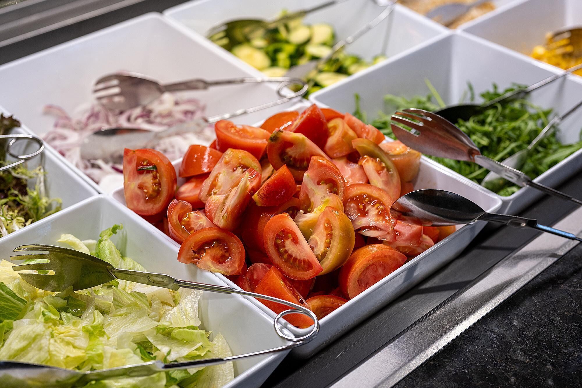 Un bufé con diversas opciones de comida, incluyendo tomates en rodajas, lechuga y otras verduras.