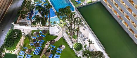 A hotel with multiple swimming pools, sun loungers, and a well-maintained lawn area.