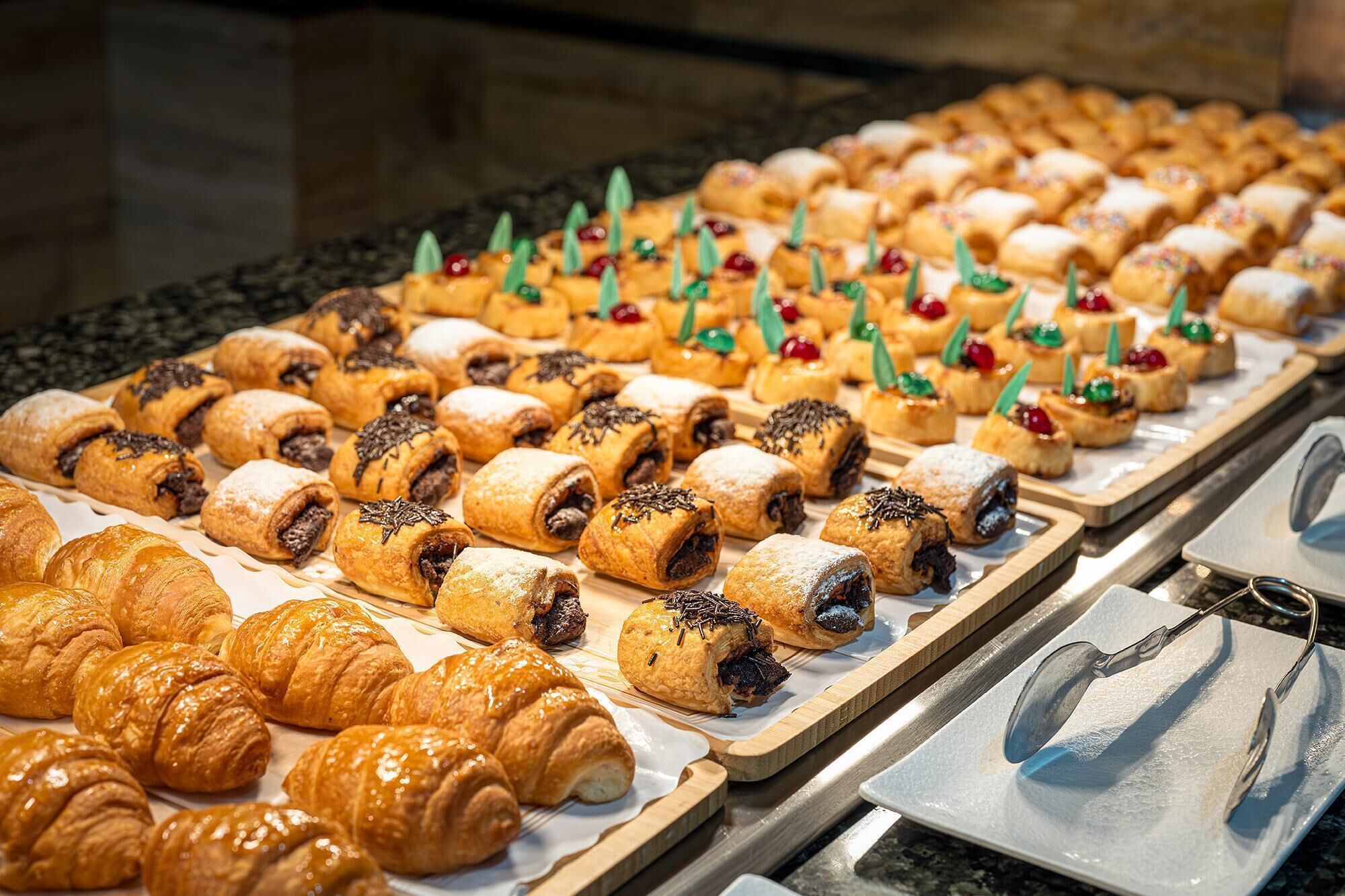 Un bufé con diversas pastas, incluyendo croissants y preparaciones rellenas, dispuestas en fuentes.