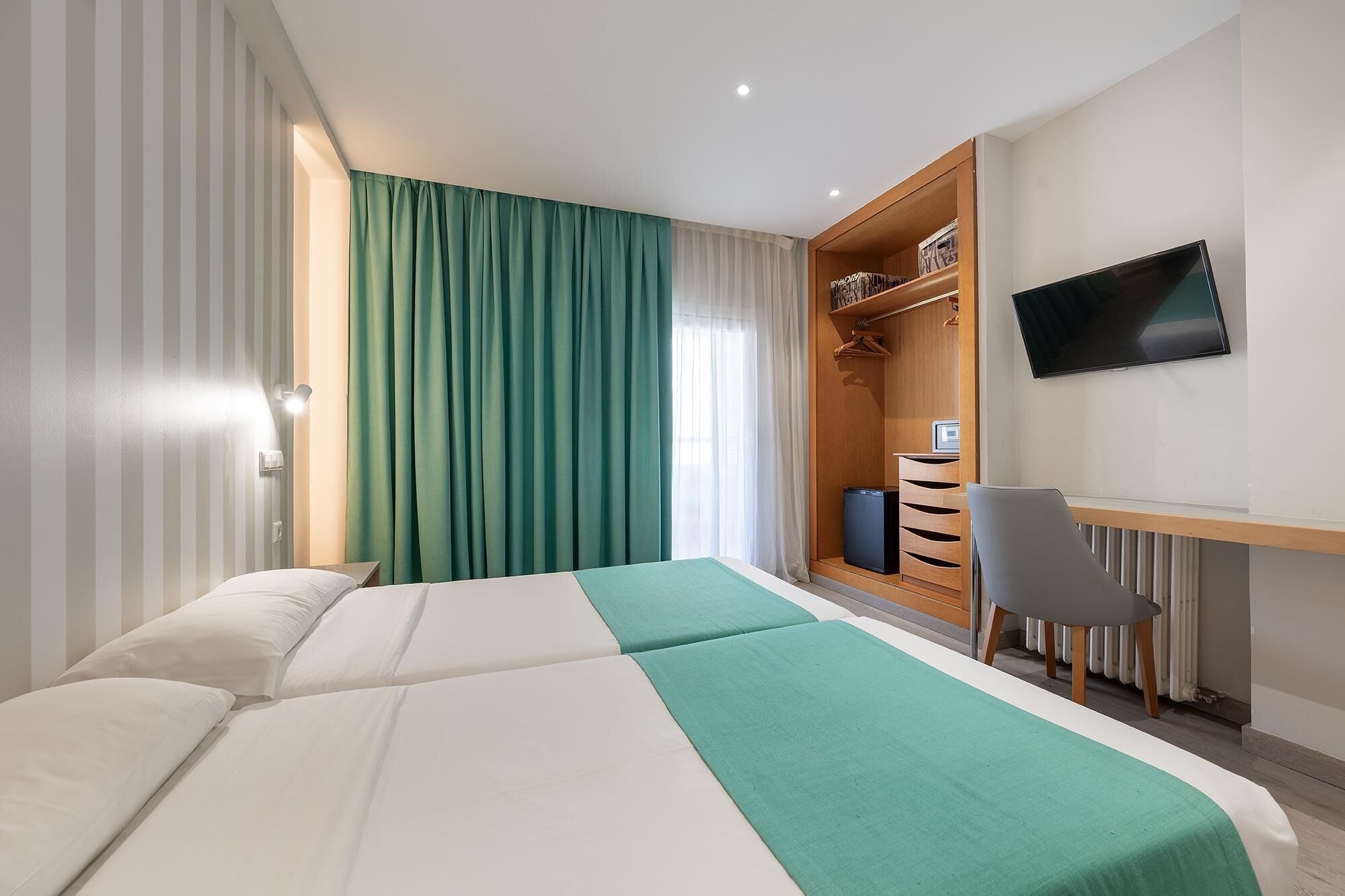 A hotel room with a bed, a desk with a chair, a television, and a wardrobe.