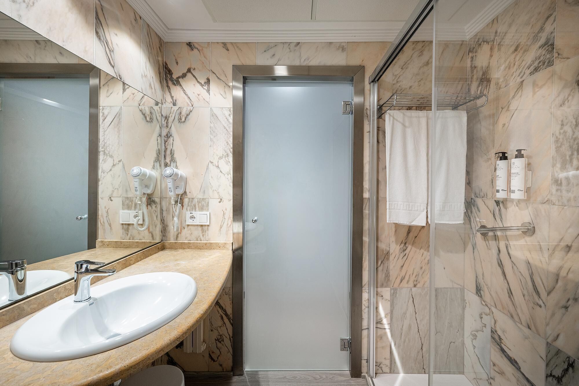 Un baño con tocador de mármol, cabina de ducha y perchero.