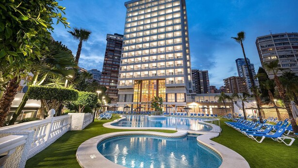A hotel with a large pool area, surrounded by palm trees and blue lounge chairs. - Poseidon Resort (Benidorm)