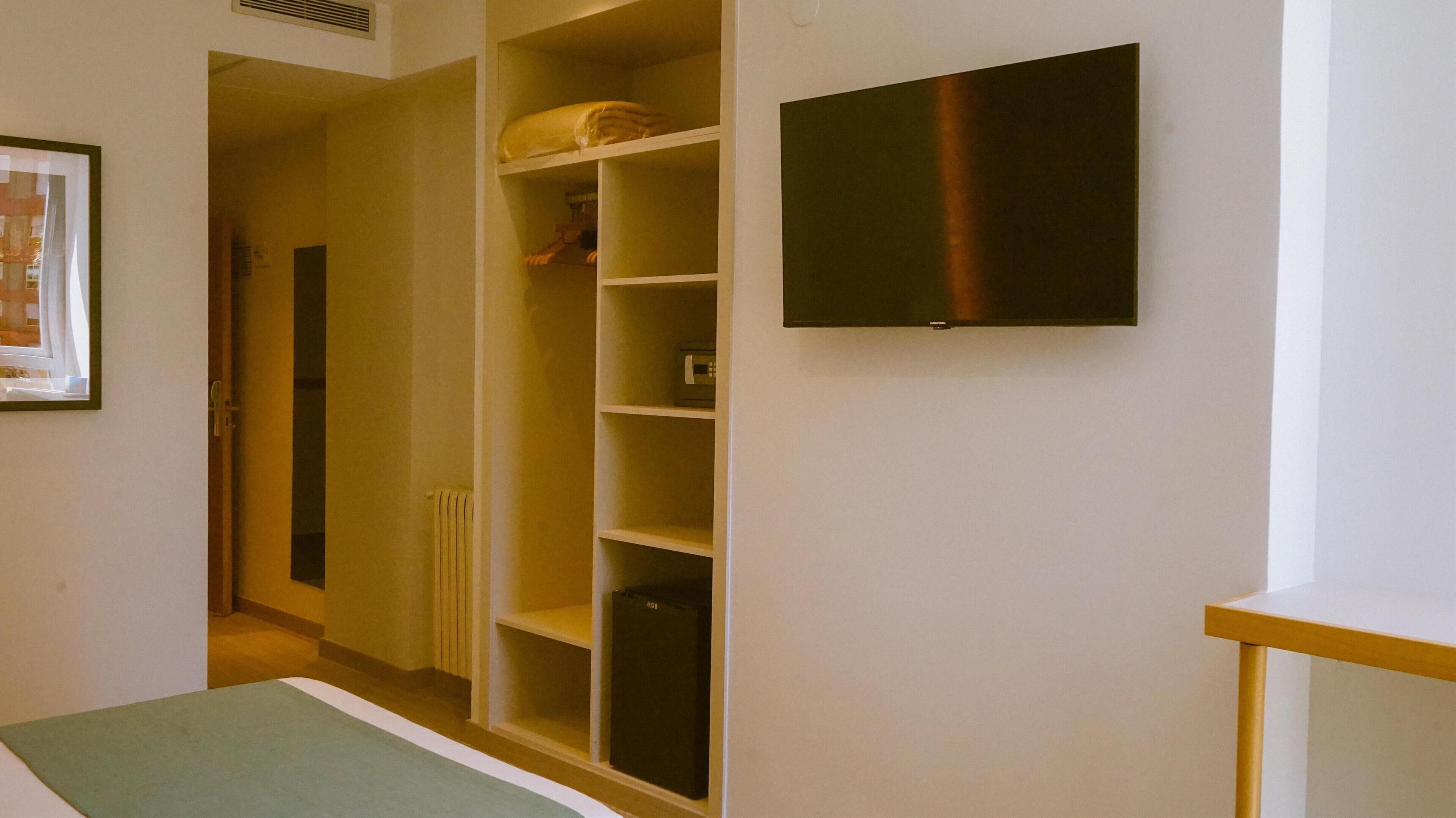 Una habitación con armario empotrado, televisor de pantalla plana en la pared y una mesita.