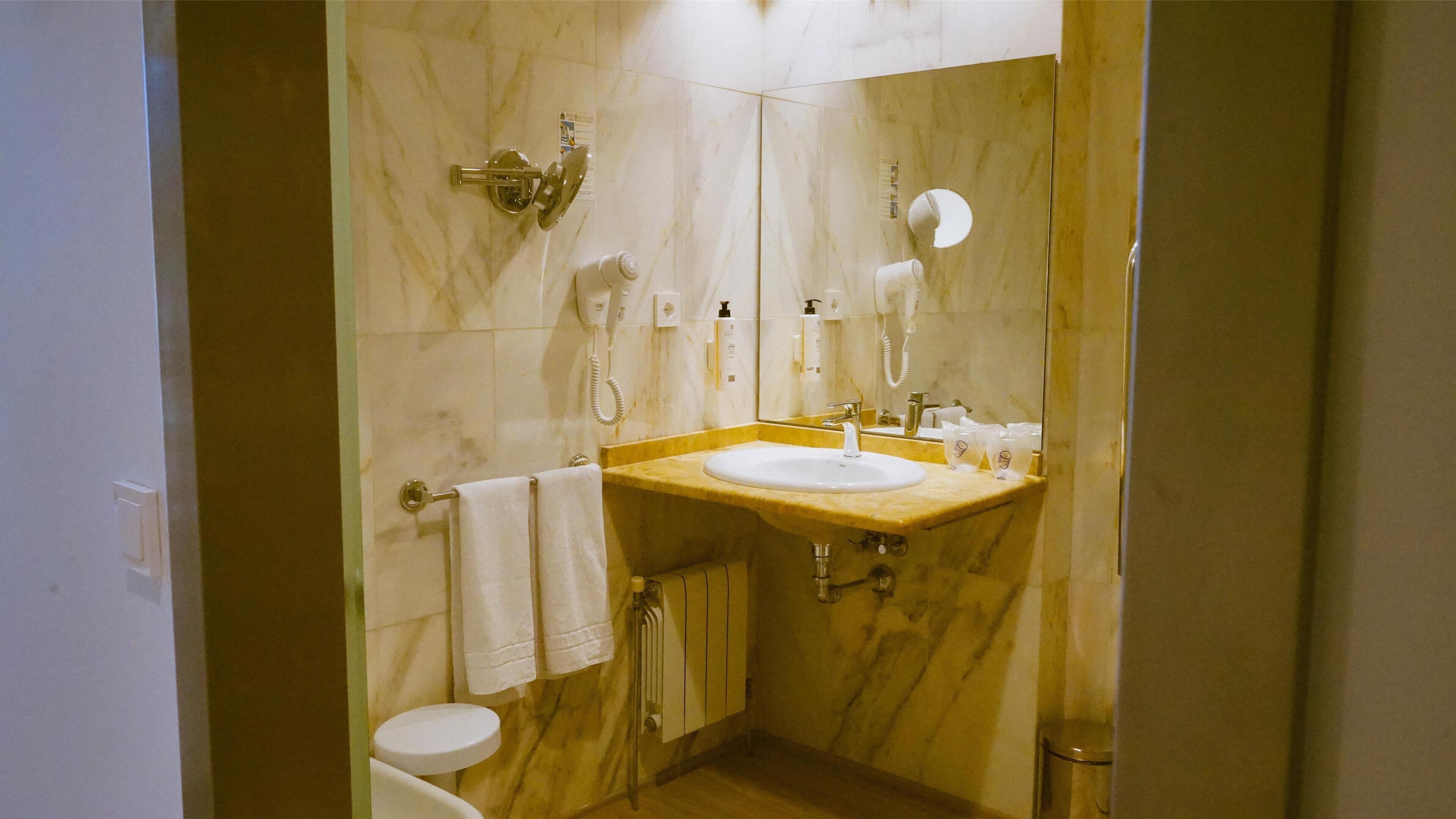 A bathroom with a marble wall, a sink with a mirror, a towel rack, a toilet, and a shower.