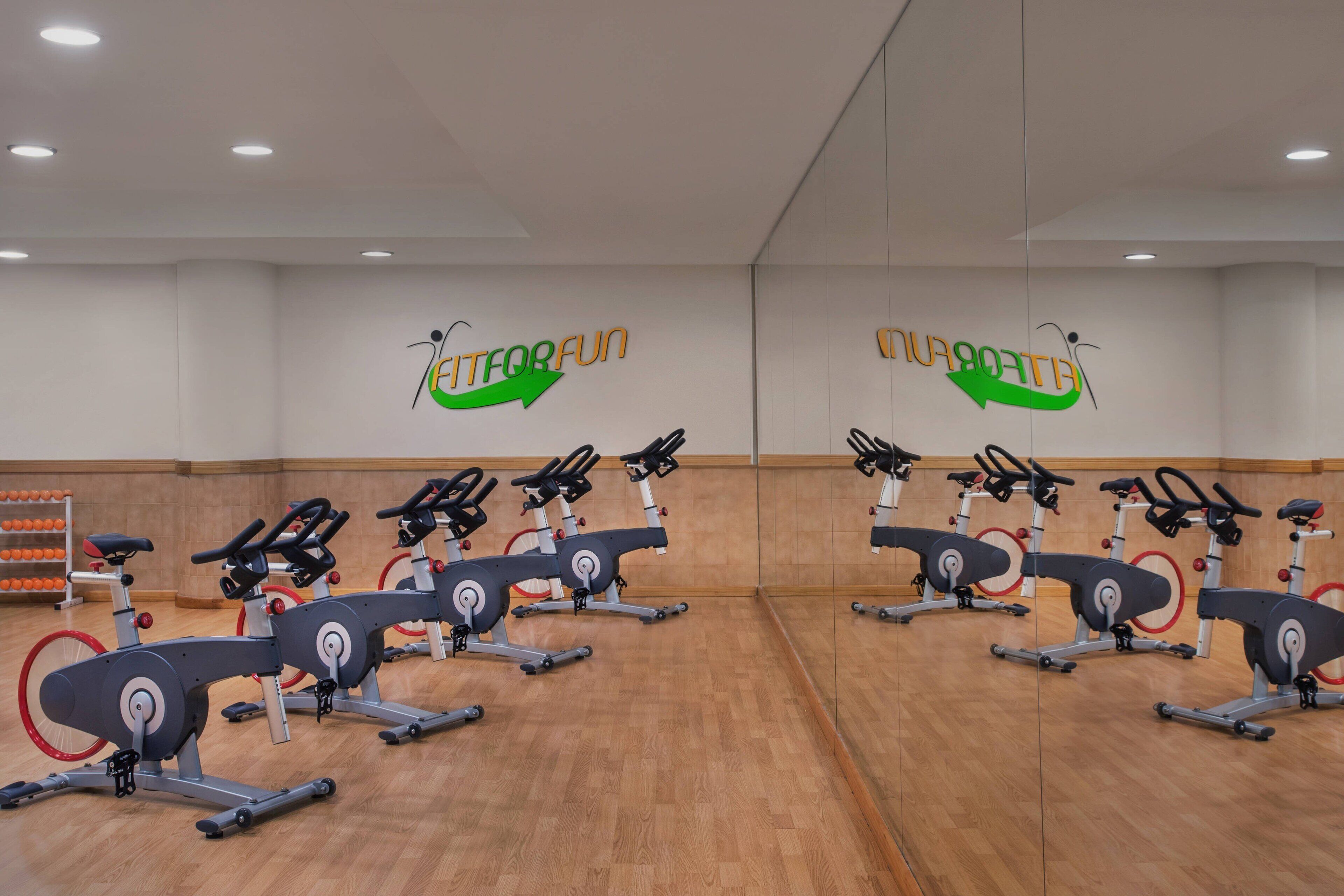 A gym with multiple stationary bikes, wooden flooring, and a mirrored wall.