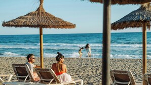 Una playa con sillas de descanso y sombrillas de paja.