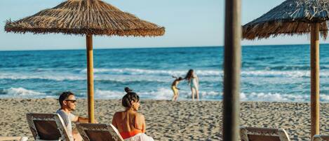 A beach with lounge chairs and thatched umbrellas.