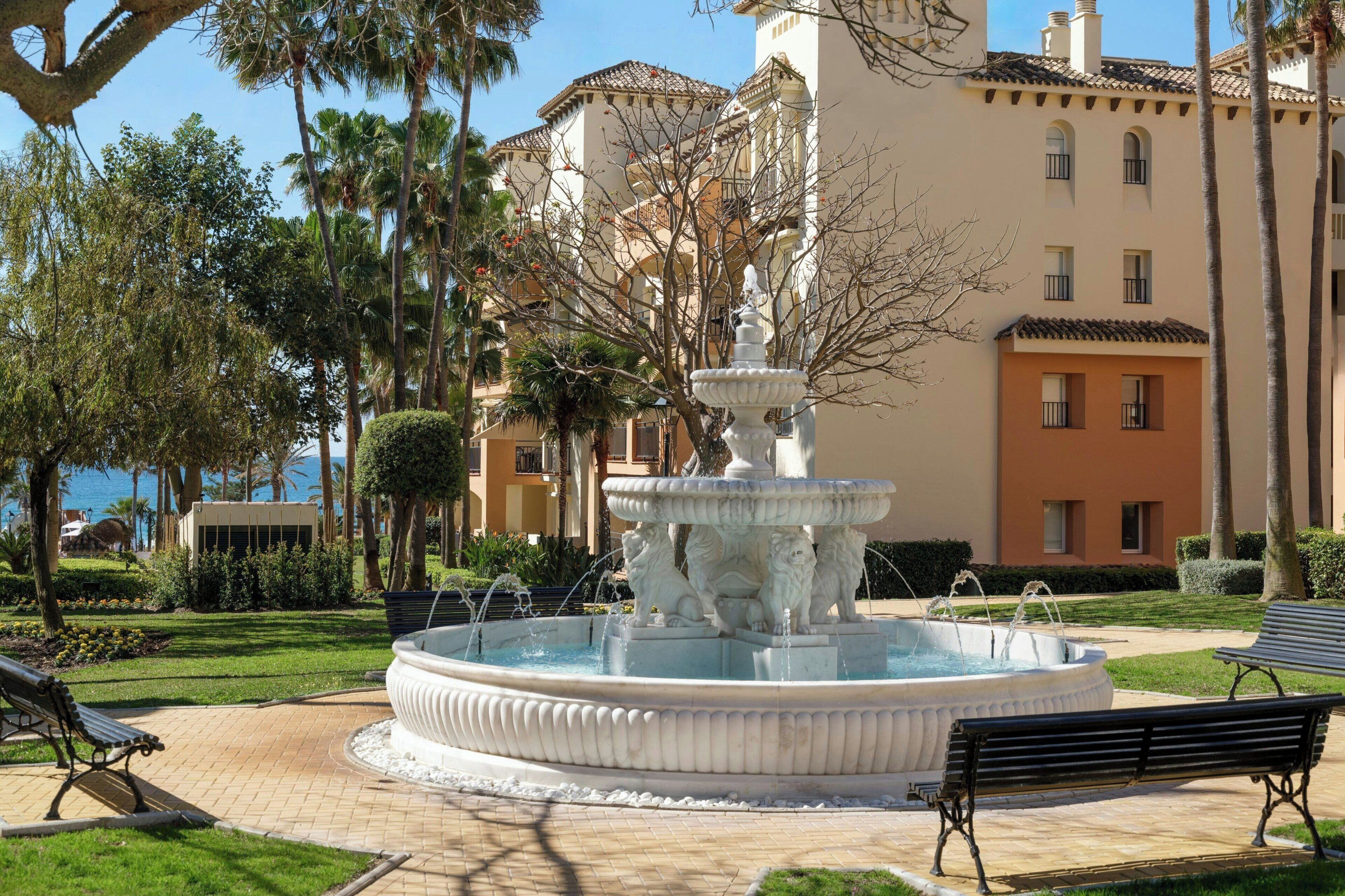 Een fontein met een trapsgewijs ontwerp, omringd door een verhard gebied met banken.