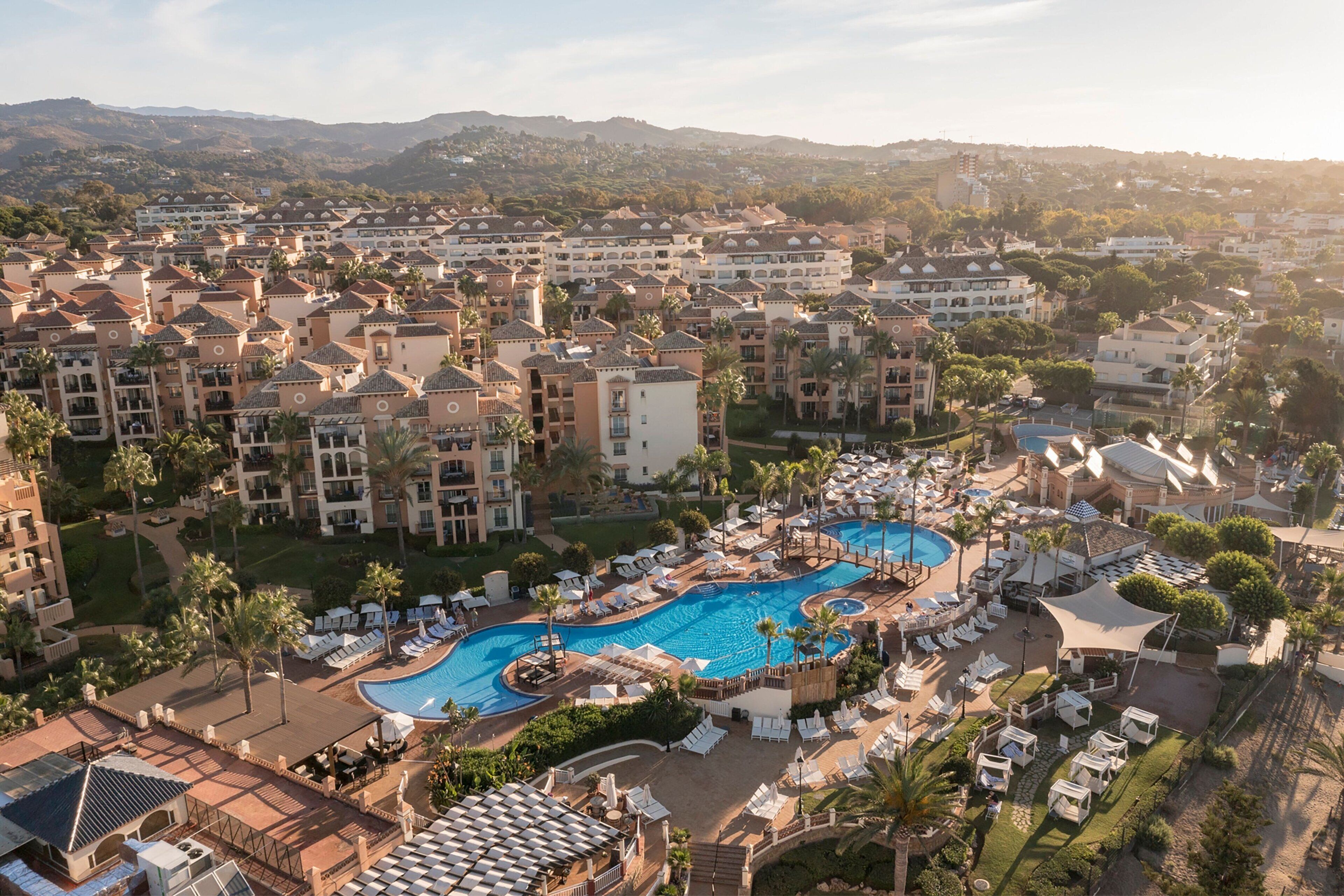 A resort with multiple buildings, a central swimming pool, and surrounding lounge areas.