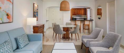 A living room with a sofa, chairs, a coffee table, a dining table, and a kitchen area with cabinets and a sink.