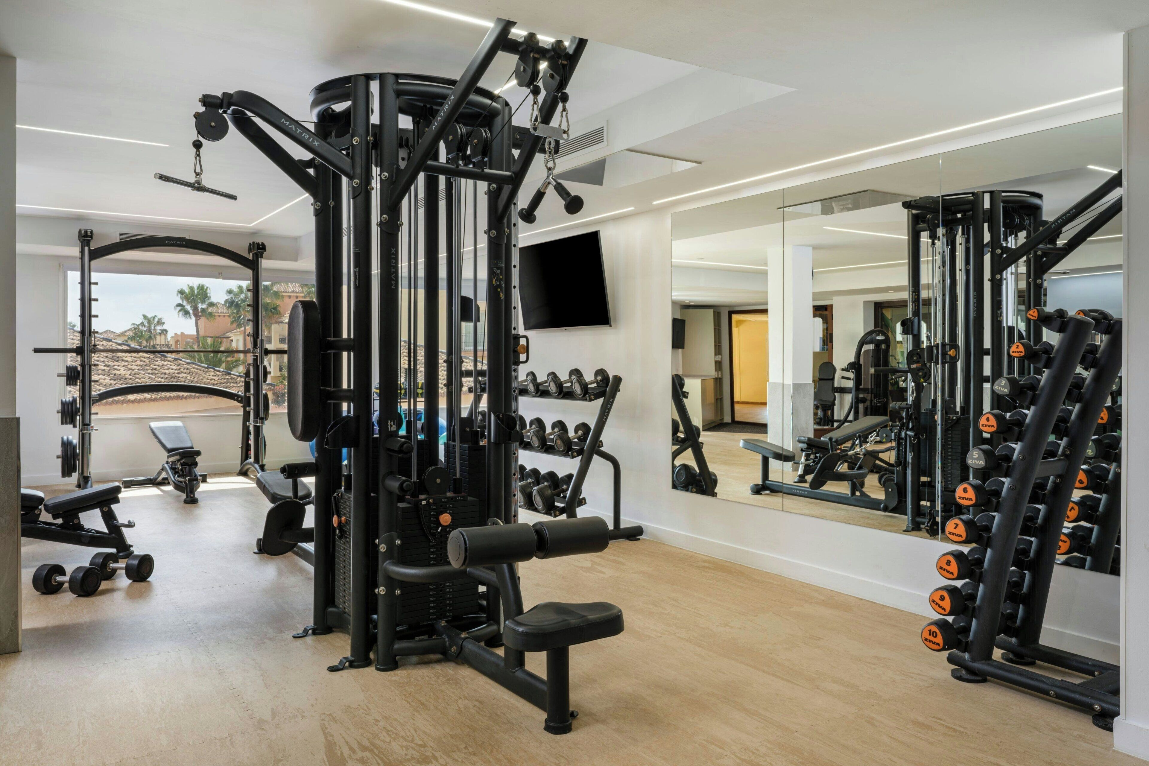 A gym with various exercise equipment, a bench, and a wall-mounted TV.