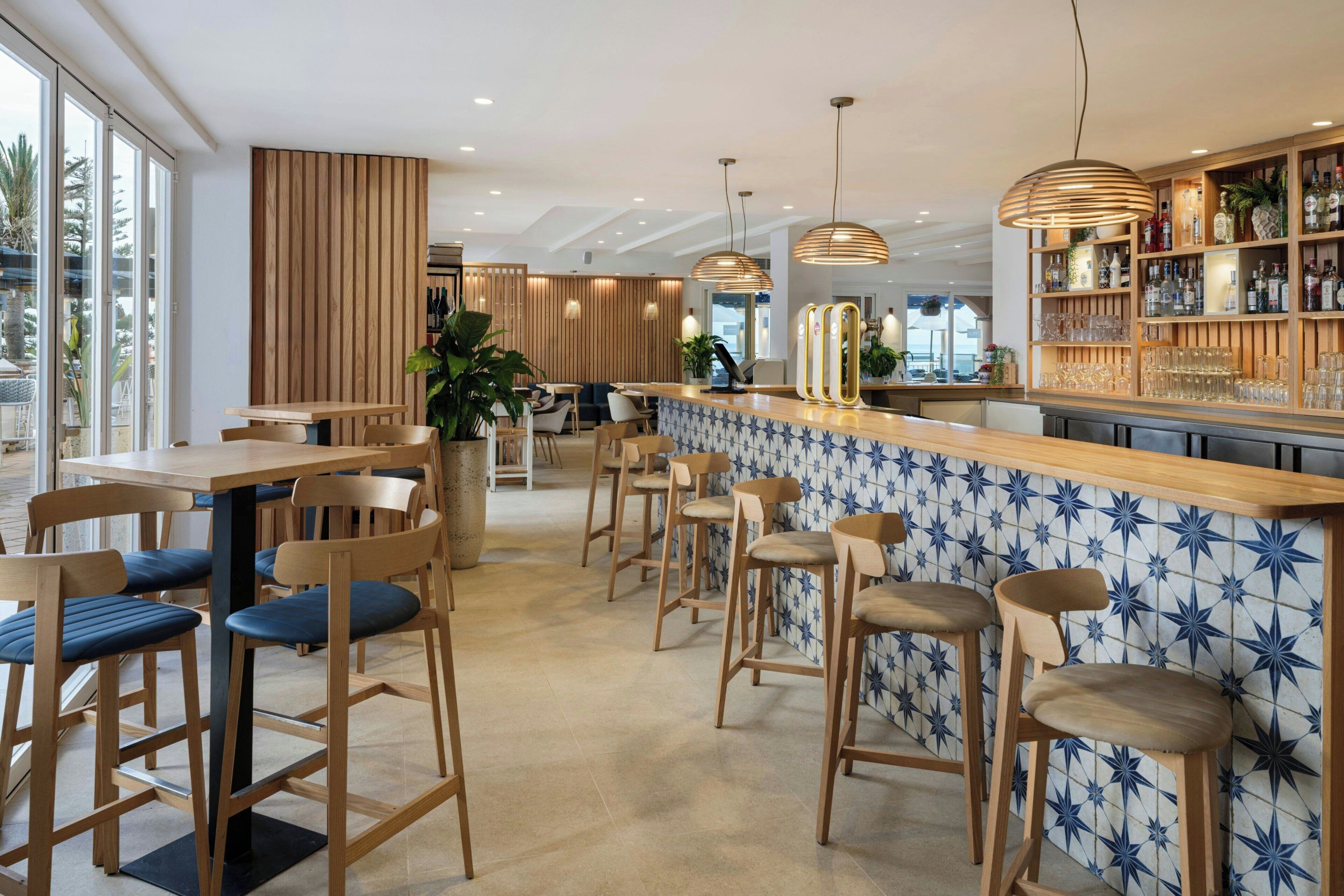 A modern bar area with wooden furniture, a tiled backsplash, and a variety of bottles and glasses on shelves.