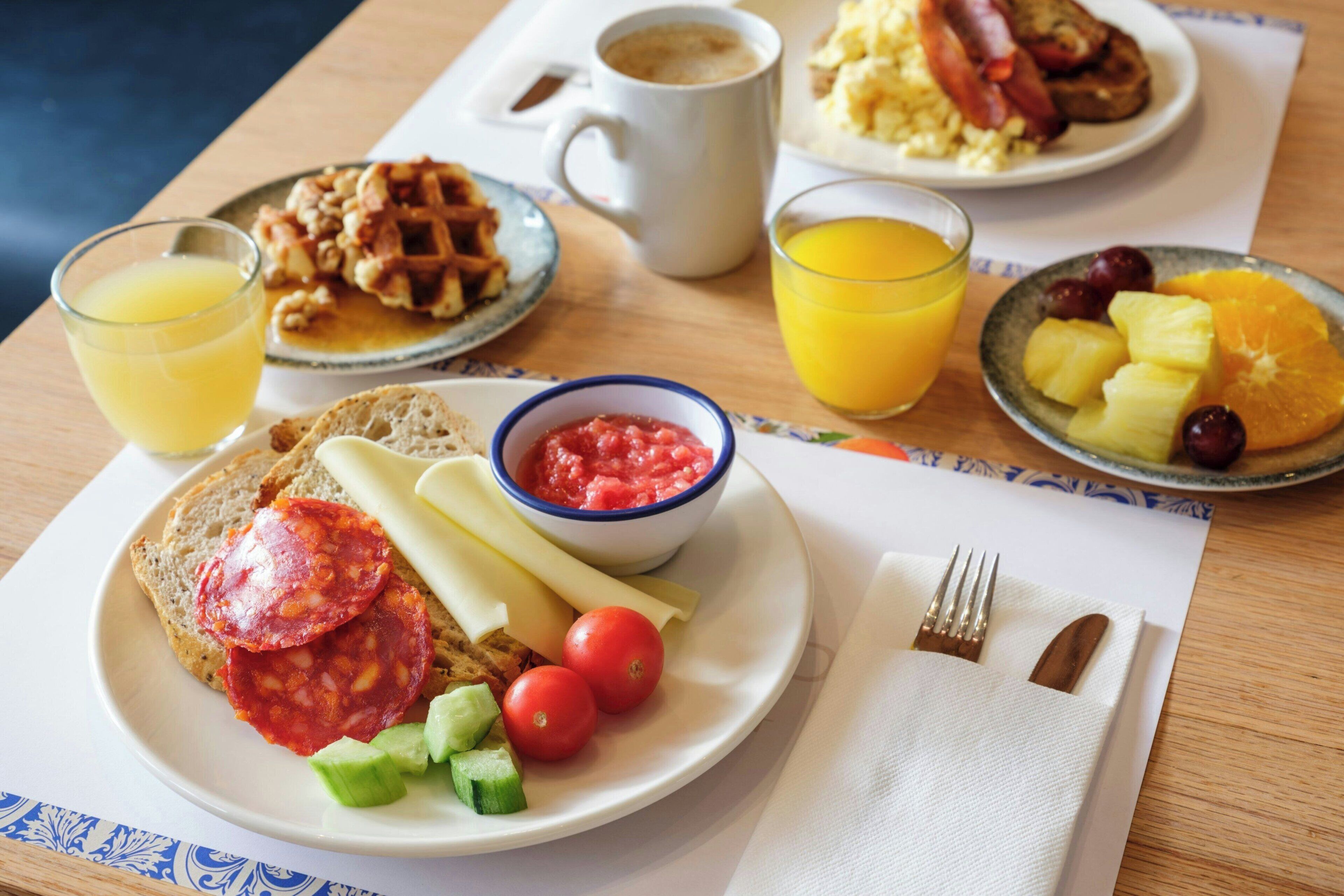 A breakfast table with plates of food, a coffee mug, and glasses of orange juice.