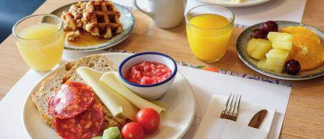 Une table de petit-déjeuner avec des assiettes remplies de nourriture, une tasse de café et des verres de jus d’orange.