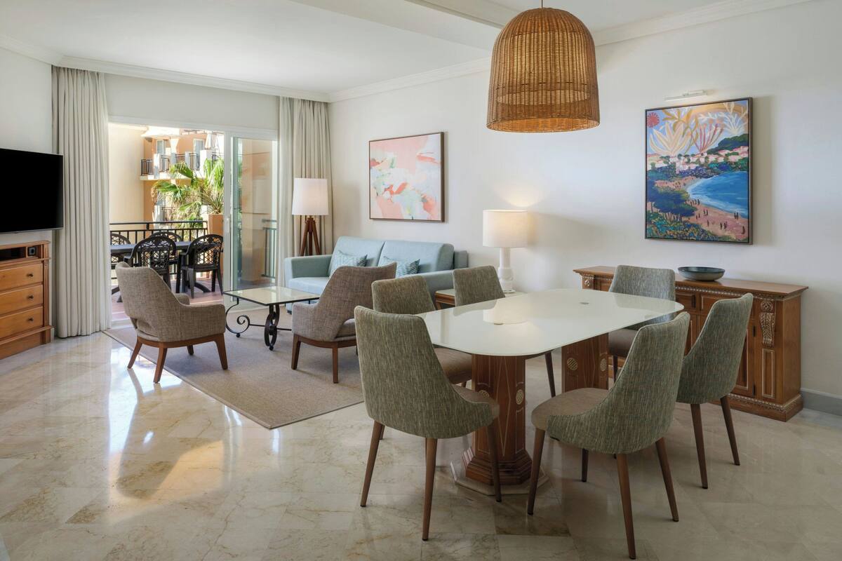 A modern living room with a dining table, chairs, a sofa, a TV, and artwork on the walls.