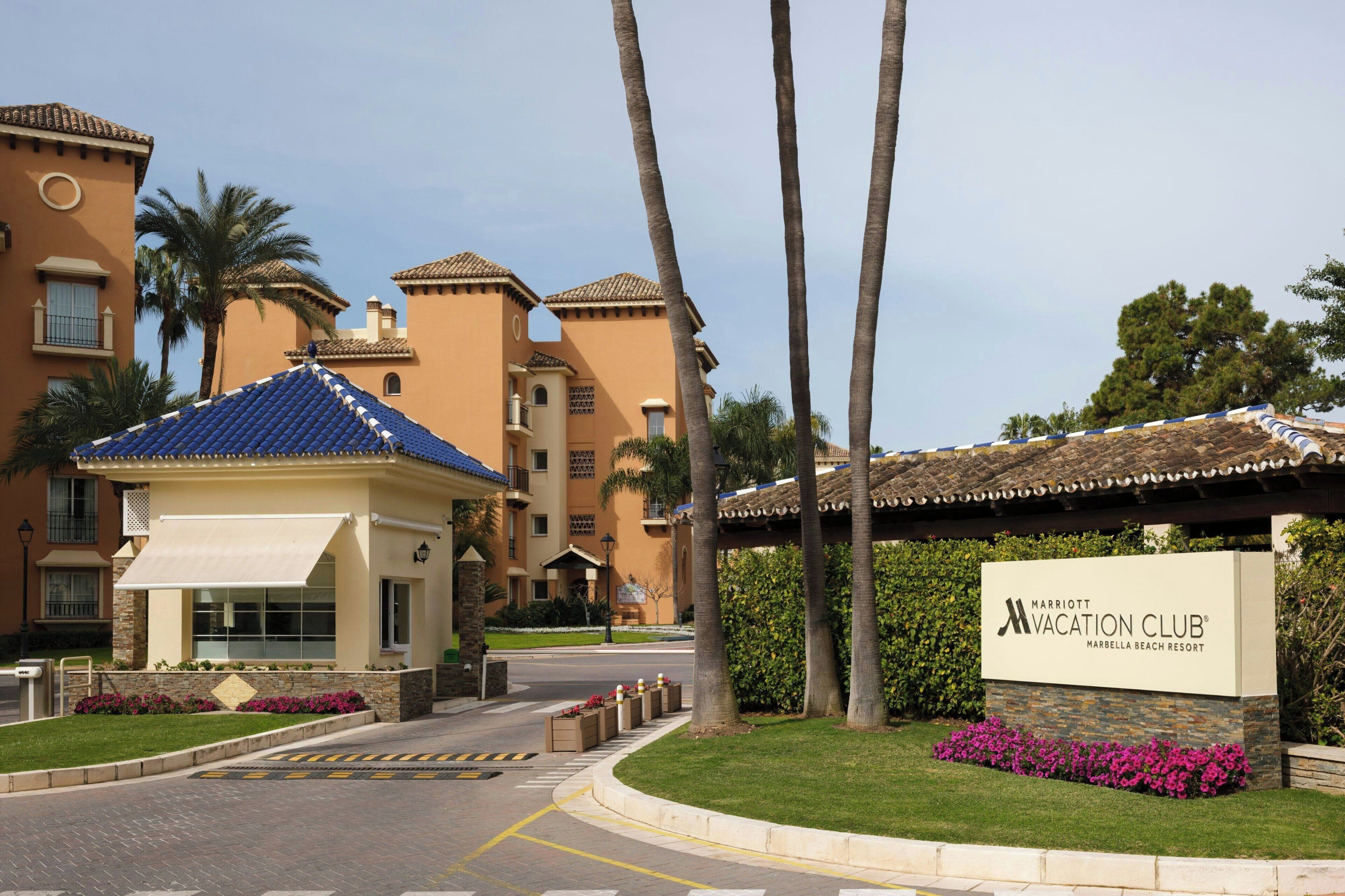 A resort with a sign for the Marriott Vacation Club, featuring a building with a blue roof, palm trees, and a well-maintained lawn.